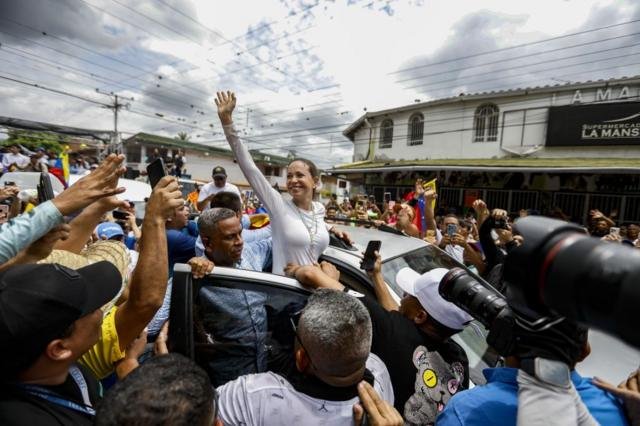 María Corina Machado saluda desde la puerta de un auto a sus seguidores.