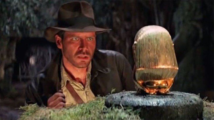 Harrison Ford como Indiana Jones mirando a un ídolo dorado en "En busca del arca perdida".