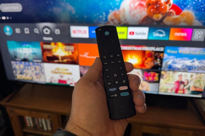 Una mano sosteniendo el control remoto de Amazon Fire TV frente al televisor Omni Mini-LED de Amazon Fire TV.