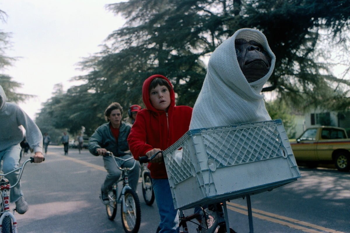un niño manejando bicicleta y un extraterreste montado en la bicicleta
