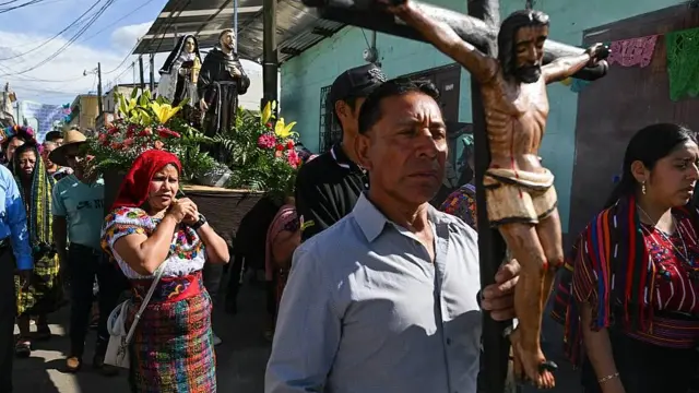 Procesión en Guatemala pidiendo por la lluvia. En la imagen se ve a pobladores con ropas coloridas tradicionales llevando un crucifijo de madera y estatuas de santos